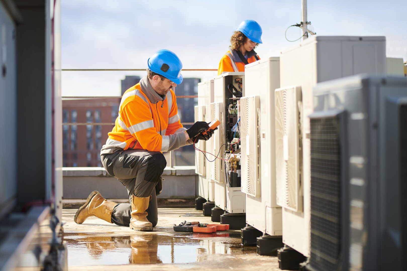Two workers in safety gear inspecting rooftop equipment.