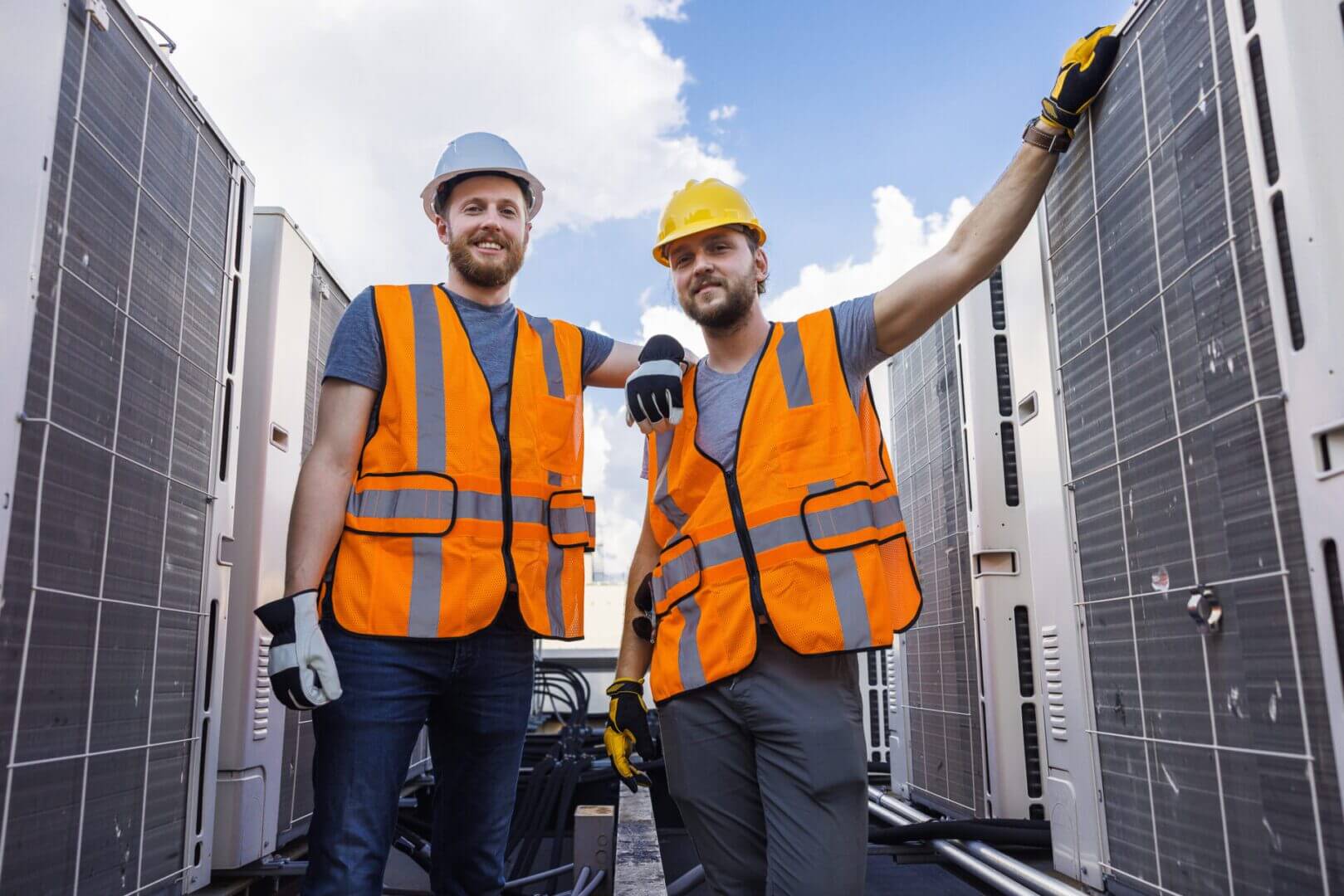 Two construction workers in safety gear standing on a rooftop.
