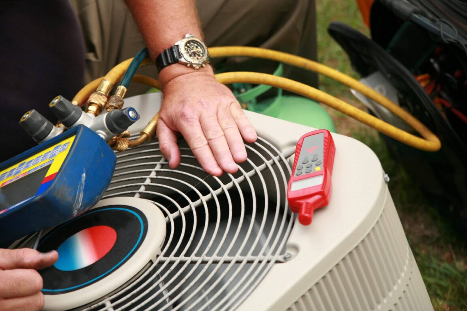 Technician's hand checking an air conditioning unit's fan with a multimeter.