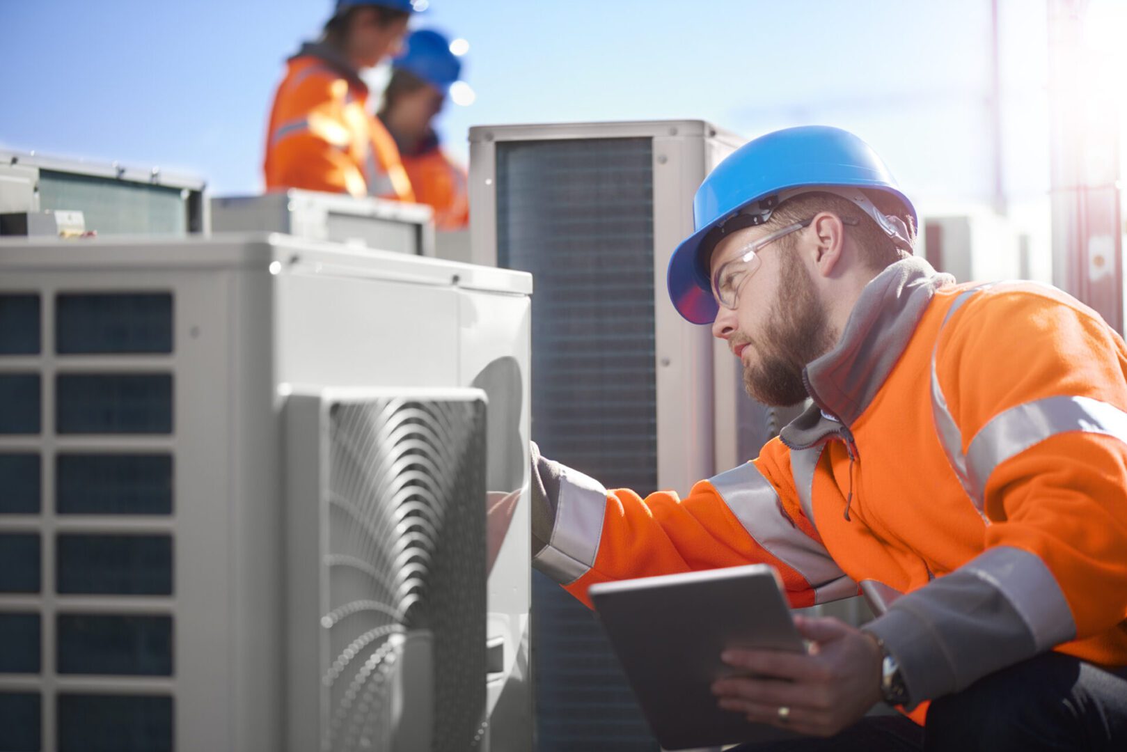 Worker in safety gear inspects electrical equipment outdoors.